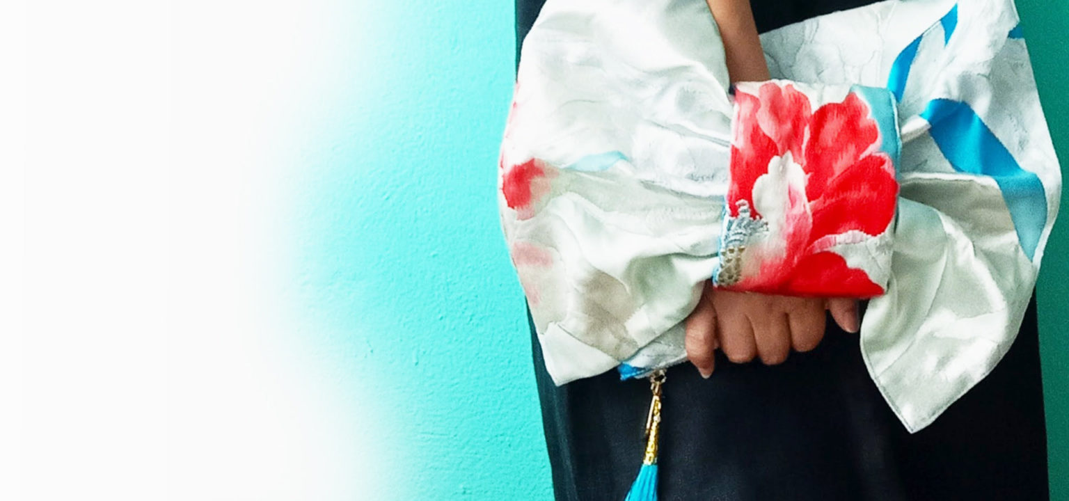 Kimono clutch bag with a red peony, held against a turquoise wall