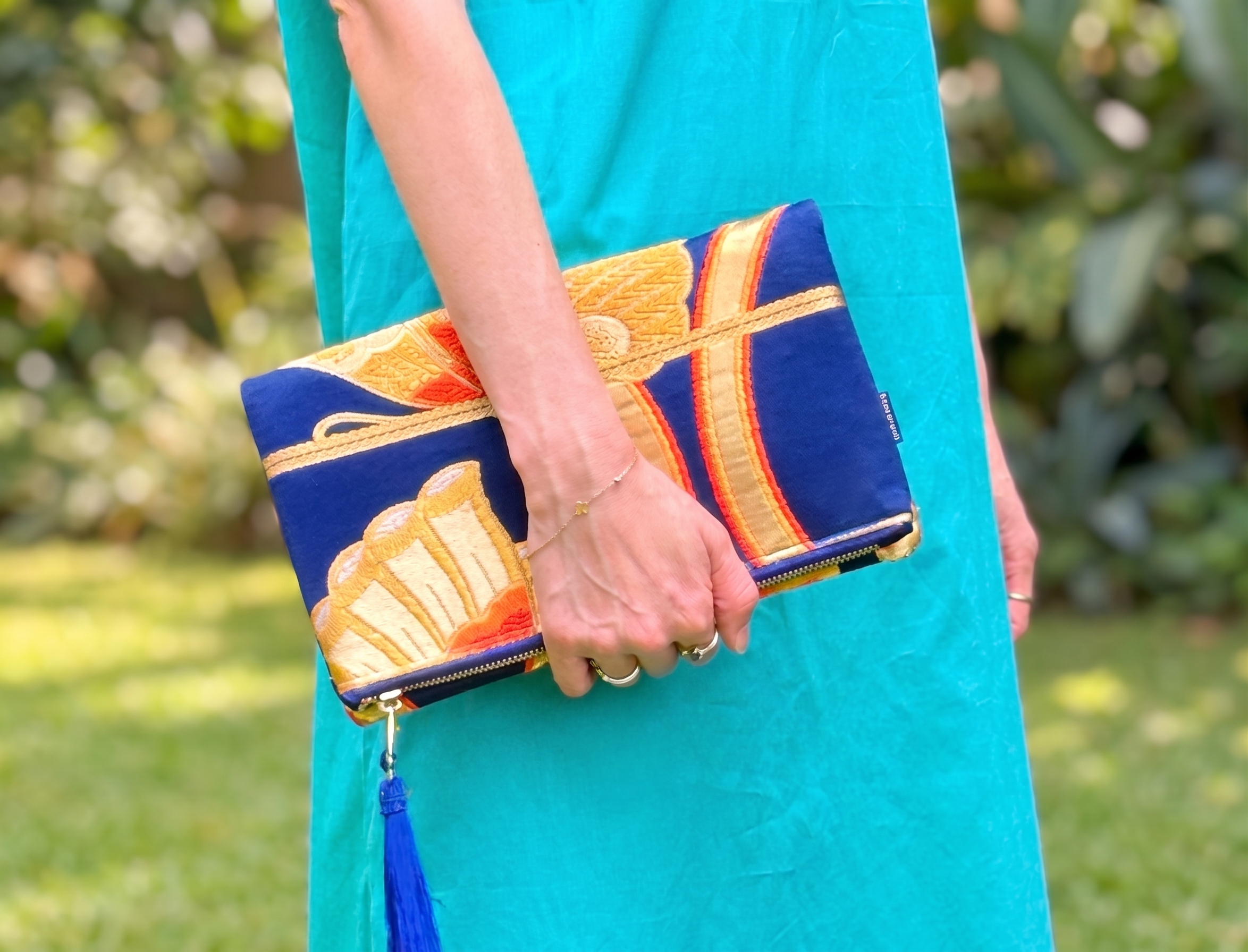Kimono clutch bag with a red peony, held against a turquoise wall